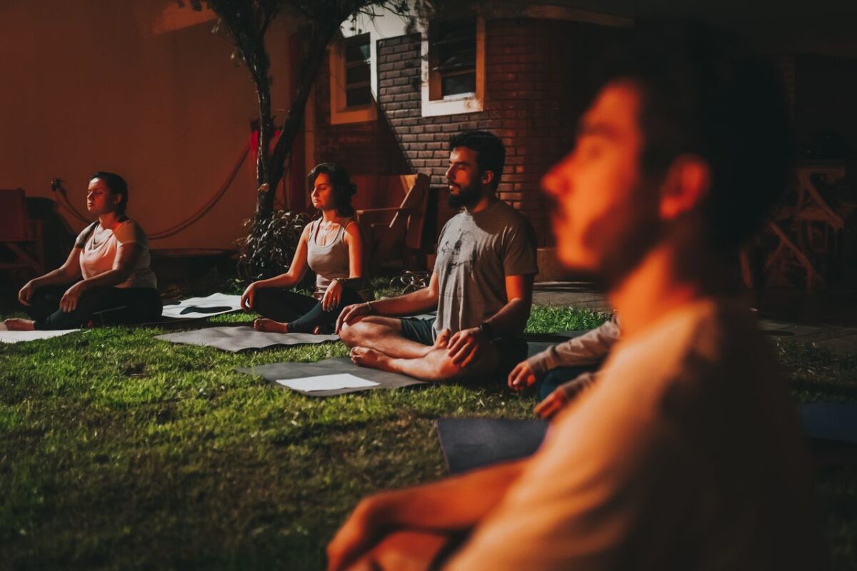 about-02 A group of people practicing yoga meditation outdoors at dusk in a peaceful garden setting.