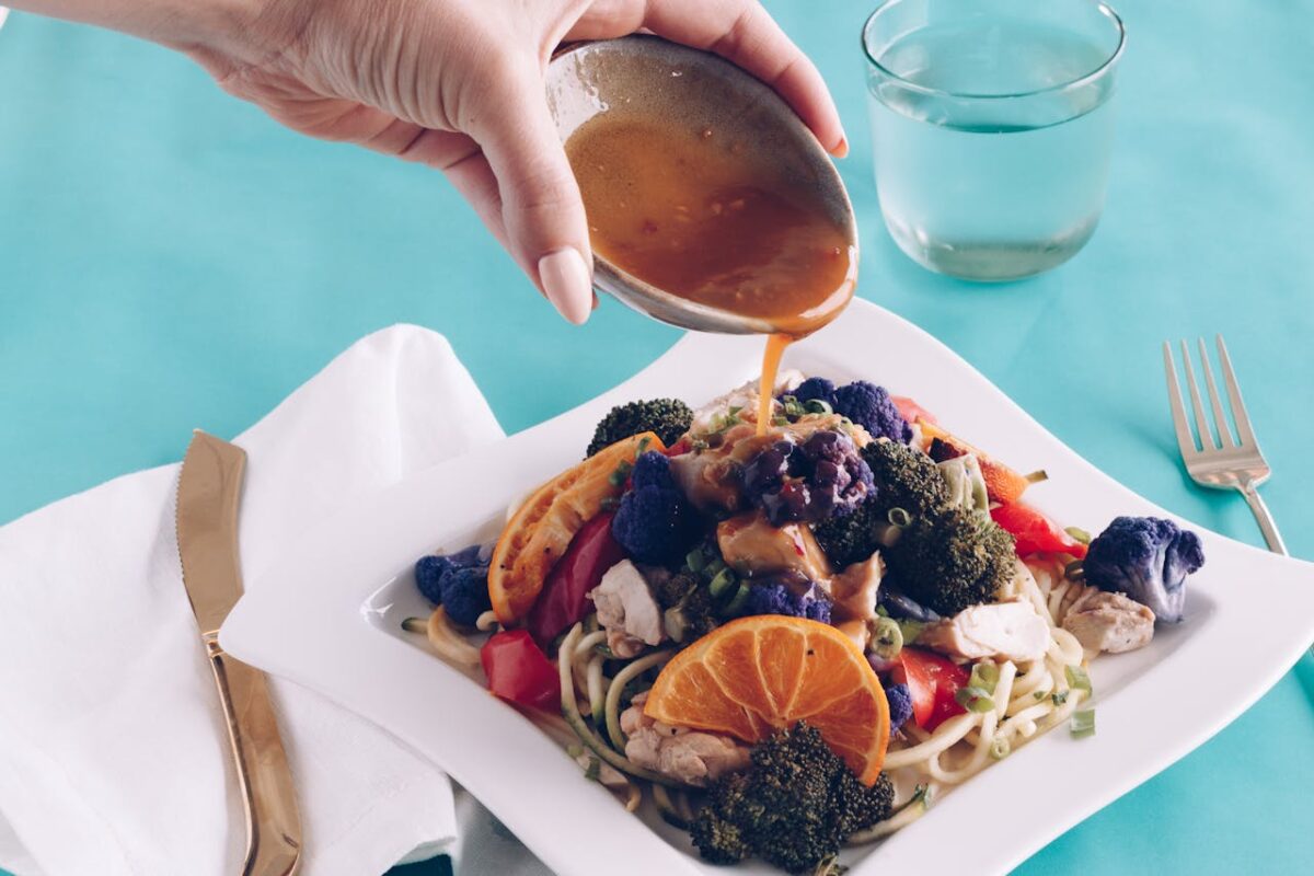 about-01 Healthy dish with veggies and sauce being poured on noodles, showcasing bright colors.